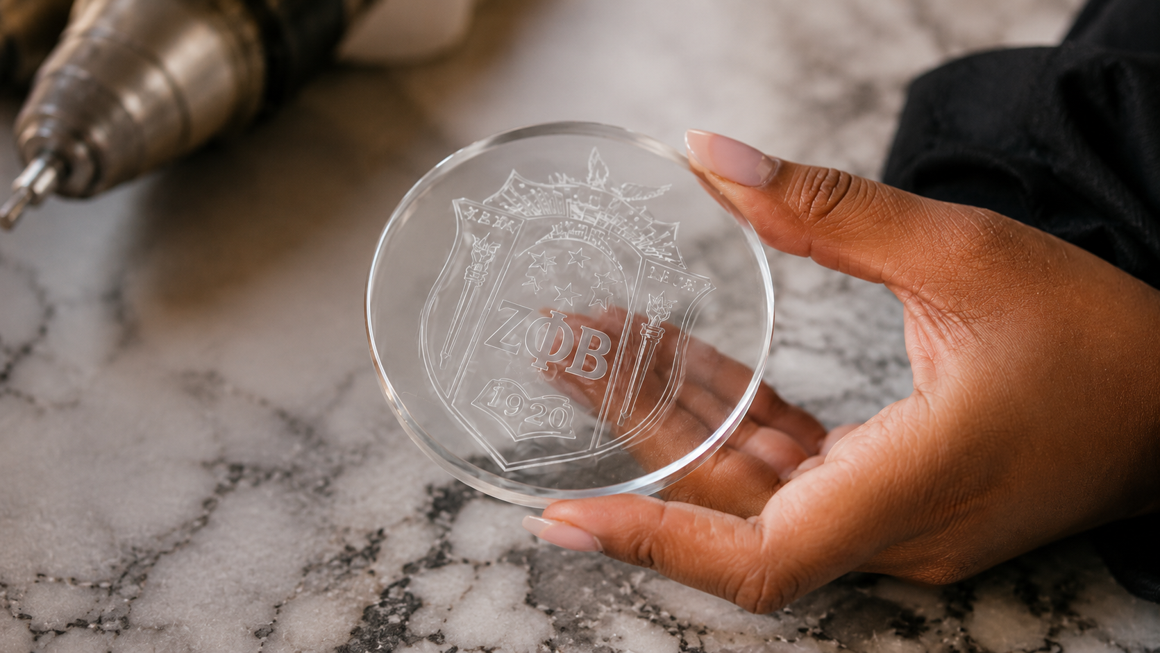 Hand-held ΦΚΨ etched coaster on marble — studio atmosphere